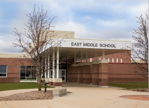 A white roofed walk way leading into the tan East Middle school building