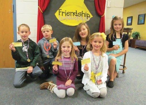 Kids gleefully holding yellow notes in front of a wall reading friendship