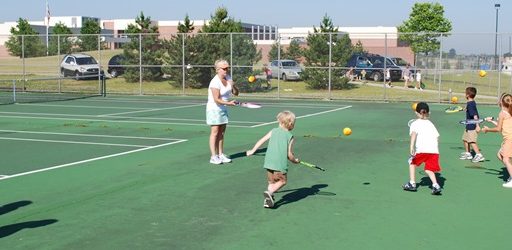 Kids bounce tennis balls off their rackets on the court
