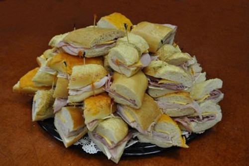 A black dish of bite side sandwiches, held together in the center by a toothpick